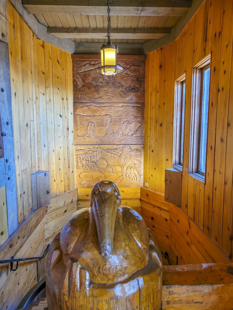 Newel post carving with Oregon Trail relief panels behind it at Timberline Lodge
