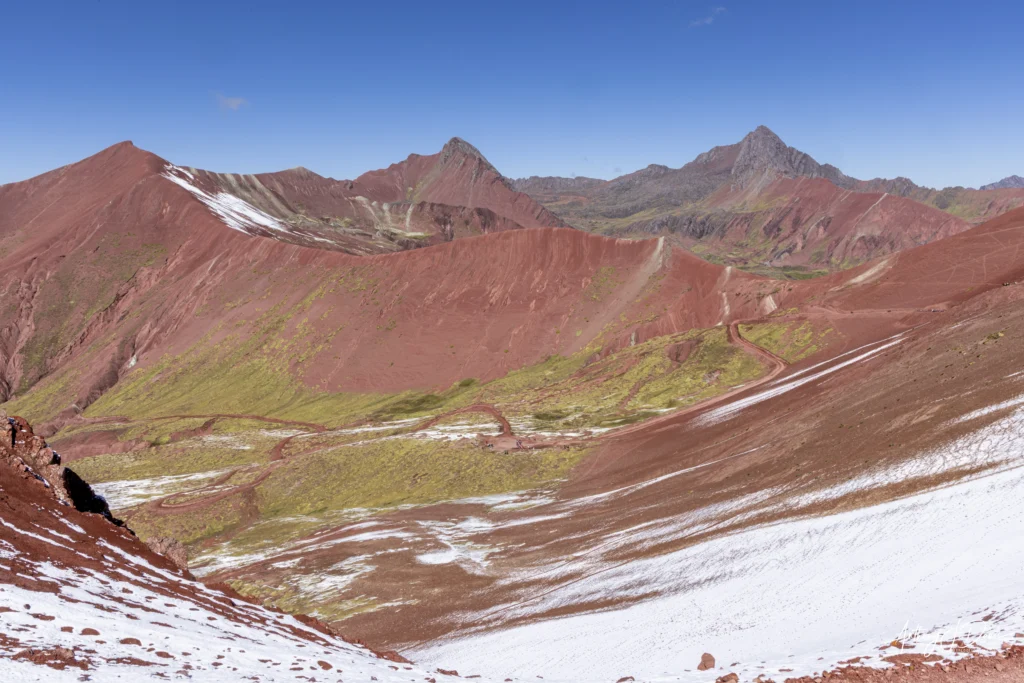 Panoramic view of Red Valley beneath a clear blue sky with patches of snow and a winding dirt trail.